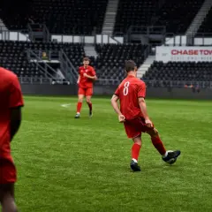 Jugadores de fútbol en uniforme rojo practicando ejercicios de pases en un campo verde, con gradas vacías al fondo.