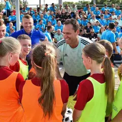 Un entrenador UEFA C, con una sonrisa, habla con un grupo de niños y niñas futbolistas.