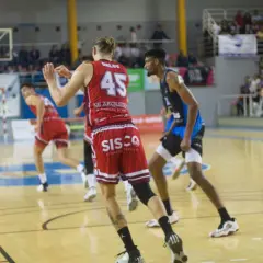 Jugadores de baloncesto en acción, con el balón en el aire y el marcador visible. Se vislumbran puntos de baloncesto en el juego.