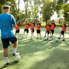 Entrenador supervisa a niños practicando sus football skills en un campo verde.