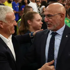 Dos entrenadores, uno con traje oscuro y corbata, el otro con traje azul, se saludan. Podría ser un momento de tensión o respeto mutuo tras un partido entre España y Francia.