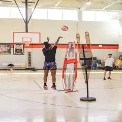 Jugadora de baloncesto practica sus posiciones de defensa en cancha, lanzando a canasta entre figuras de entrenamiento.