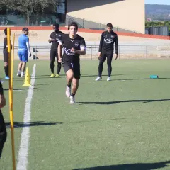 Jóvenes futbolistas realizan pruebas físicas en campo. Un entrenador de fútbol nivel 1 supervisa el entrenamiento.