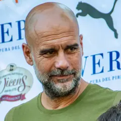 Pep Guardiola, con su mirada reflexiva, parece estar en un evento de "pep guardiola estudios". Detrás, logos de "Veri" y "Vicens".