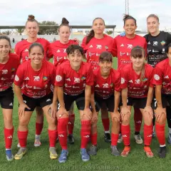 Equipo de fútbol femenino posando en el campo. Las jugadoras, con camisetas rojas y negras, muestran su espíritu deportivo.