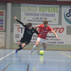 Jugadores de fútbol sala compiten por el balón. Uno viste de negro, el otro de rojo, ambos con calcetines altos. El partido se desarrolla en una cancha interior con publicidad de "cd bargas" y otros patrocinadores.