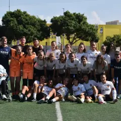 Equipo de fútbol femenino del Massanassa CF posa en el campo, con entrenadores y una persona en silla de ruedas.