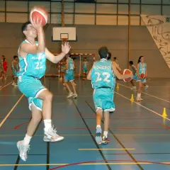 Jugadores de baloncesto realizan ejercicios analíticos en cancha. Uno salta para lanzar, otro dribla.