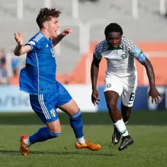 Jugadores de fútbol en acción, uno con camiseta blanca y verde de la **selección Nigeria**, el otro con azul.