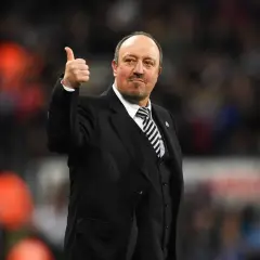 Rafa Benítez, con traje y corbata a rayas, da el pulgar hacia arriba. Su trayectoria con diversos equipos es legendaria.