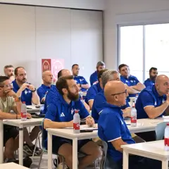 Un grupo de entrenadores España asiste a una charla en un aula, todos con polos azules.