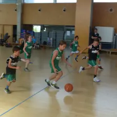 Niños practicando jugadas de baloncesto en una cancha interior.