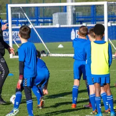 Entrenador explica a niños cómo ser un buen entrenador de futbol en un campo de entrenamiento.