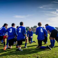 Equipo de fútbol con camisetas azules, arrodillados en el campo, preparándose para juegos de activación.