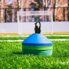 Conos de entrenamiento de fútbol apilados en césped verde, listos para una sesión. ¿Cuánto dura un entrenamiento de fútbol?