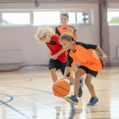 Niños jugando al baloncesto en una cancha interior. La edad infantil es clave para aprender este deporte.