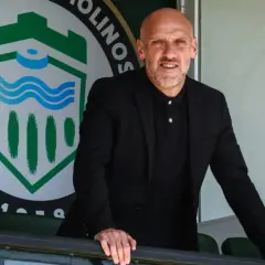 David Cabello, entrenador, posa con confianza frente al escudo de un club deportivo.