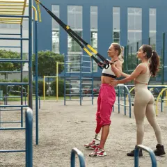 Dos mujeres entrenan en un gimnasio al aire libre. Una usa un sistema de entrenamiento en suspensión para un microciclo de impacto.