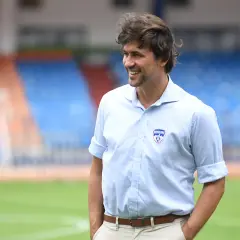 Carles Cuadrat sonríe en un campo de fútbol con gradas al fondo.