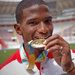 Andy Martínez, atleta peruano, muerde su medalla de oro, símbolo de su victoria en el estadio.