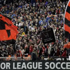 Aficionados ondean banderas rojas y negras en un partido de la liga futbol eeuu.