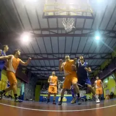 Jugadores de baloncesto compiten por un rebote bajo la canasta en un gimnasio.