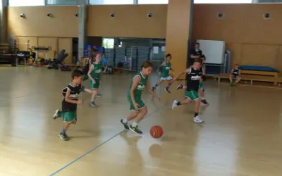 Niños practicando jugadas de baloncesto en una cancha interior.