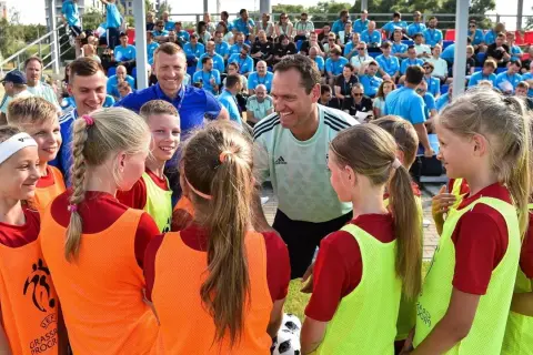 Un entrenador UEFA C, con una sonrisa, habla con un grupo de niños y niñas futbolistas.