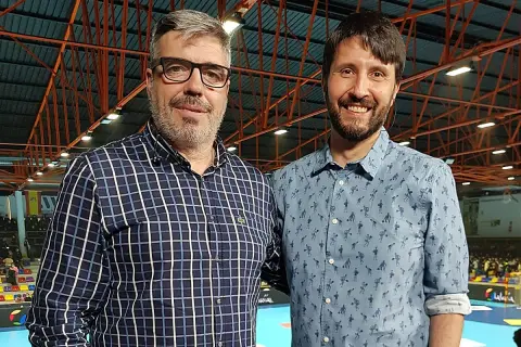 Dos hombres sonríen a la cámara. El de la izquierda, con gafas y camisa a cuadros, es Paco Caro. El de la derecha lleva una camisa azul con un estampado divertido.