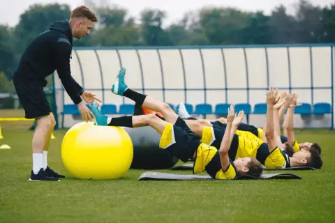 Entrenador supervisa a jóvenes futbolistas en un circuito de resistencia física.