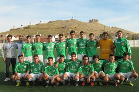 Equipo de fútbol del Atlético Consuegra posando en el campo, con molinos y castillo de fondo.