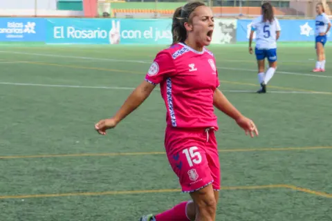 Jugadora de fútbol femenino con camiseta rosa y número 15, celebrando un gol. Las águilas femenino luchan en el campo.