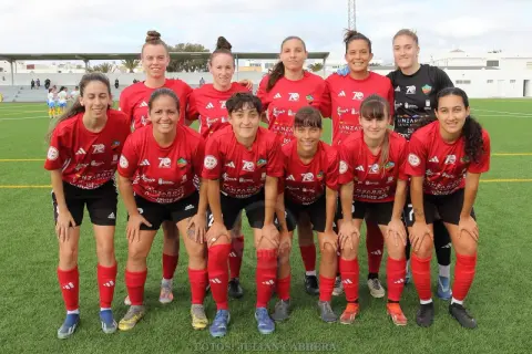 Equipo de fútbol femenino posando en el campo. Las jugadoras, con camisetas rojas y negras, muestran su espíritu deportivo.