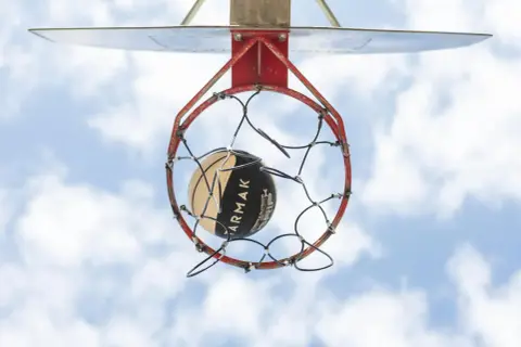 Un balón de baloncesto a punto de entrar en la canasta. La altura reglamentaria de a cuantos metros está la canasta de baloncesto del suelo es de 3.05 metros.