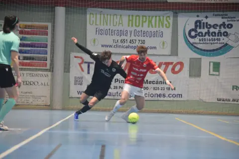 Jugadores de fútbol sala compiten por el balón. Uno viste de negro, el otro de rojo, ambos con calcetines altos. El partido se desarrolla en una cancha interior con publicidad de "cd bargas" y otros patrocinadores.