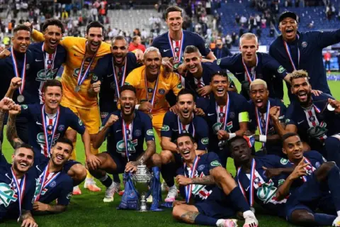 Jugadores del PSG celebran con trofeo y medallas tras ganar la liga francesa de fútbol.