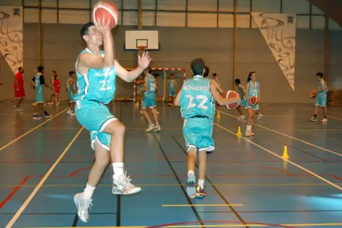 Jugadores de baloncesto realizan ejercicios analíticos en cancha. Uno salta para lanzar, otro dribla.