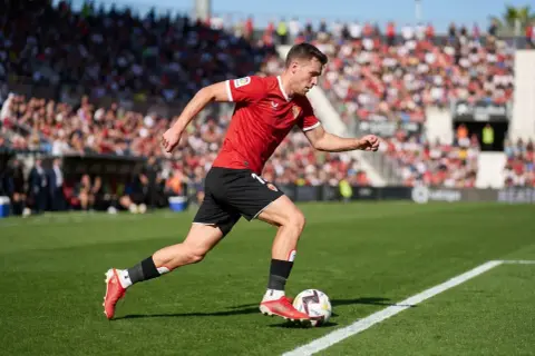 Futbolista en acción, parte de la pirámide del fútbol español, con público en las gradas.