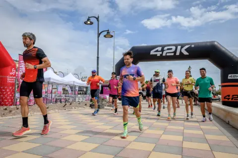 Corredores inician una carrera bajo un arco de 42K. La pregunta de cuanto dura un calentamiento se responde con la energía de estos atletas.