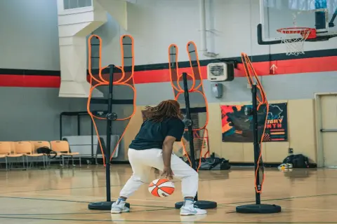 Jugador de baloncesto practica dribbling entre conos de entrenamiento en cancha interior.