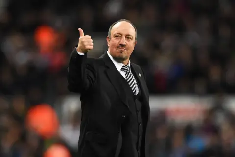 Rafa Benítez, con traje y corbata a rayas, da el pulgar hacia arriba. Su trayectoria con diversos equipos es legendaria.