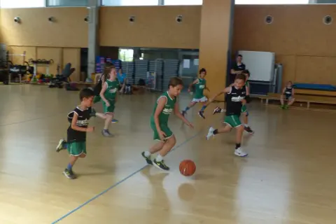 Niños practicando jugadas de baloncesto en una cancha interior.