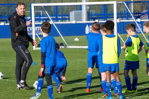 Entrenador explica a niños cómo ser un buen entrenador de futbol en un campo de entrenamiento.