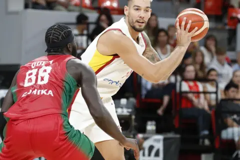 Jugador de baloncesto con el balón en mano, listo para su primera canasta de baloncesto, defendido por un oponente.