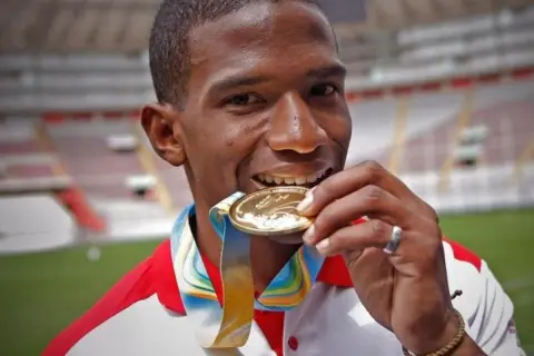 Andy Martínez, atleta peruano, muerde su medalla de oro, símbolo de su victoria en el estadio.