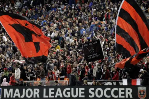 Aficionados ondean banderas rojas y negras en un partido de la liga futbol eeuu.