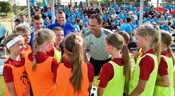 Un entrenador UEFA C, con una sonrisa, habla con un grupo de niños y niñas futbolistas.