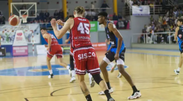 Jugadores de baloncesto en acción, con el balón en el aire y el marcador visible. Se vislumbran puntos de baloncesto en el juego.