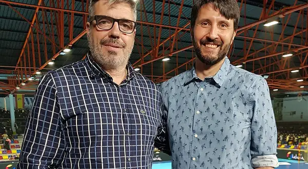 Dos hombres sonríen a la cámara. El de la izquierda, con gafas y camisa a cuadros, es Paco Caro. El de la derecha lleva una camisa azul con un estampado divertido.