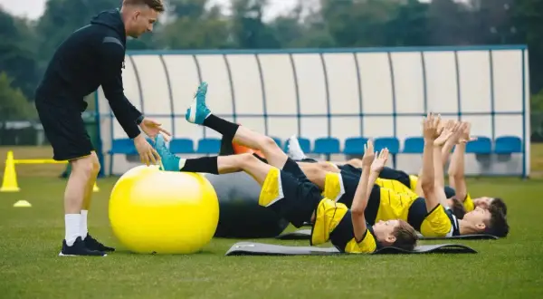 Entrenador supervisa a jóvenes futbolistas en un circuito de resistencia física.